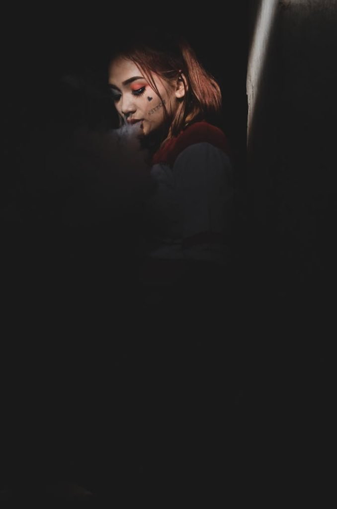 A dramatic portrait of a woman in a dimly lit room, highlighted by rim light and smoke for a cinematic effect.